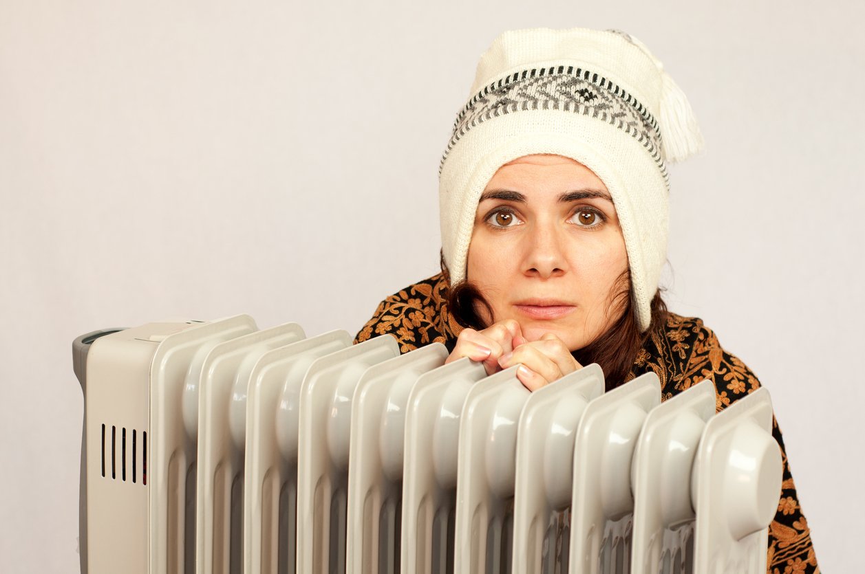 Freezing young woman near a heater