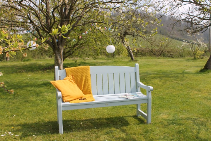 a garden bench painted grey with a yellow cushion on the left hand side